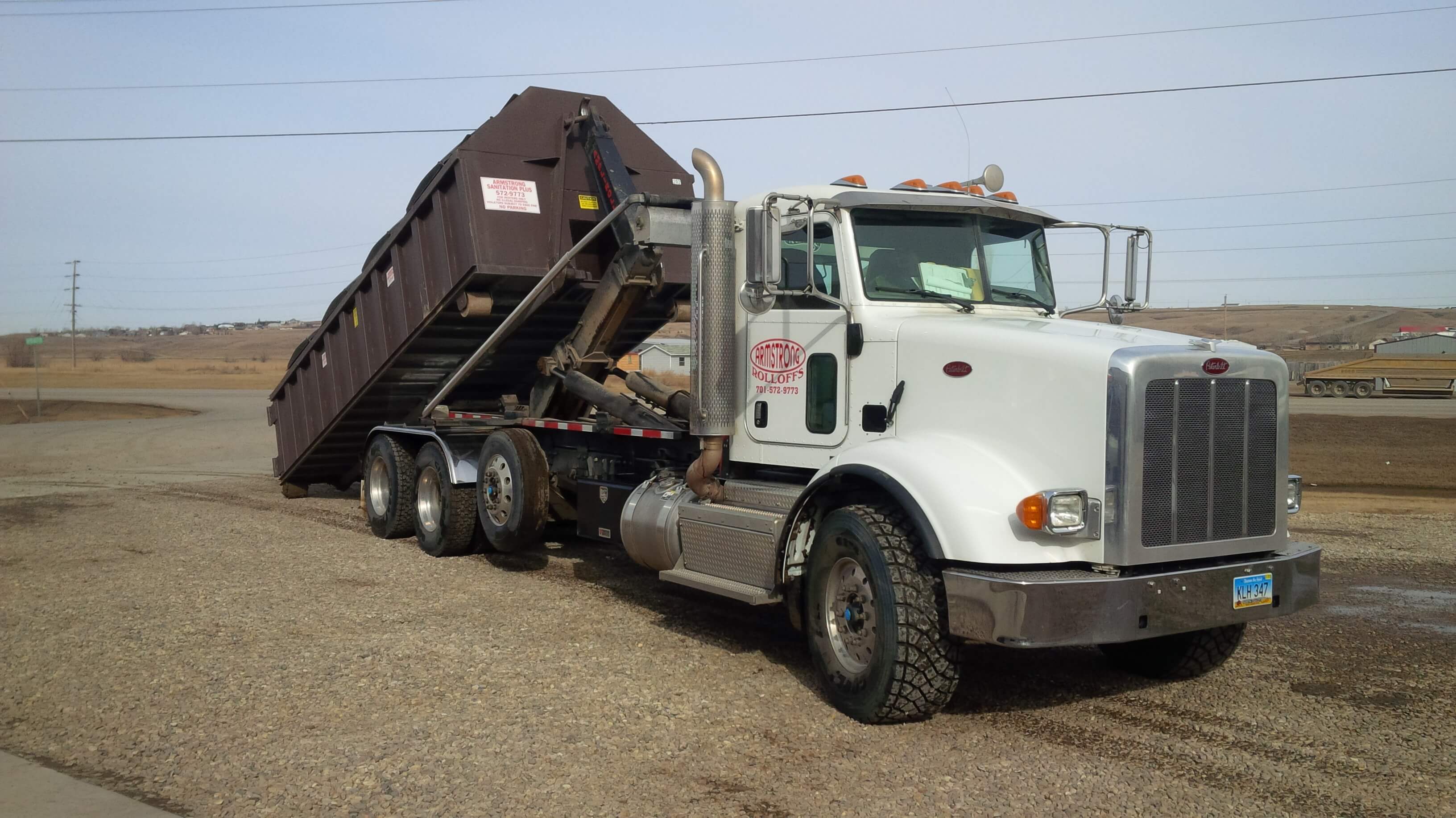 Image of Armstrong Sanitation roll-off truck unloading container.